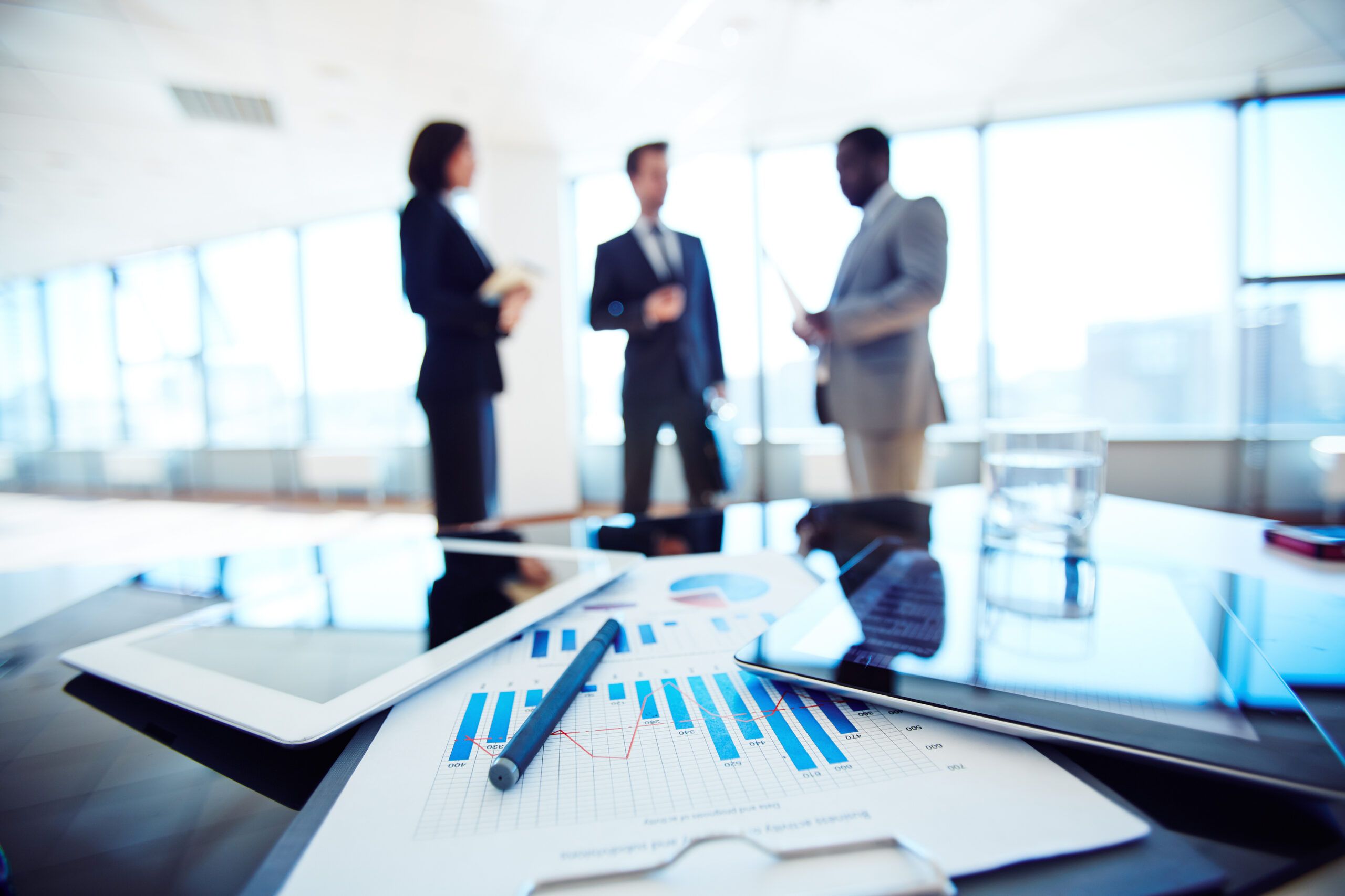 3 workers blurred in background with various business tools on the desk