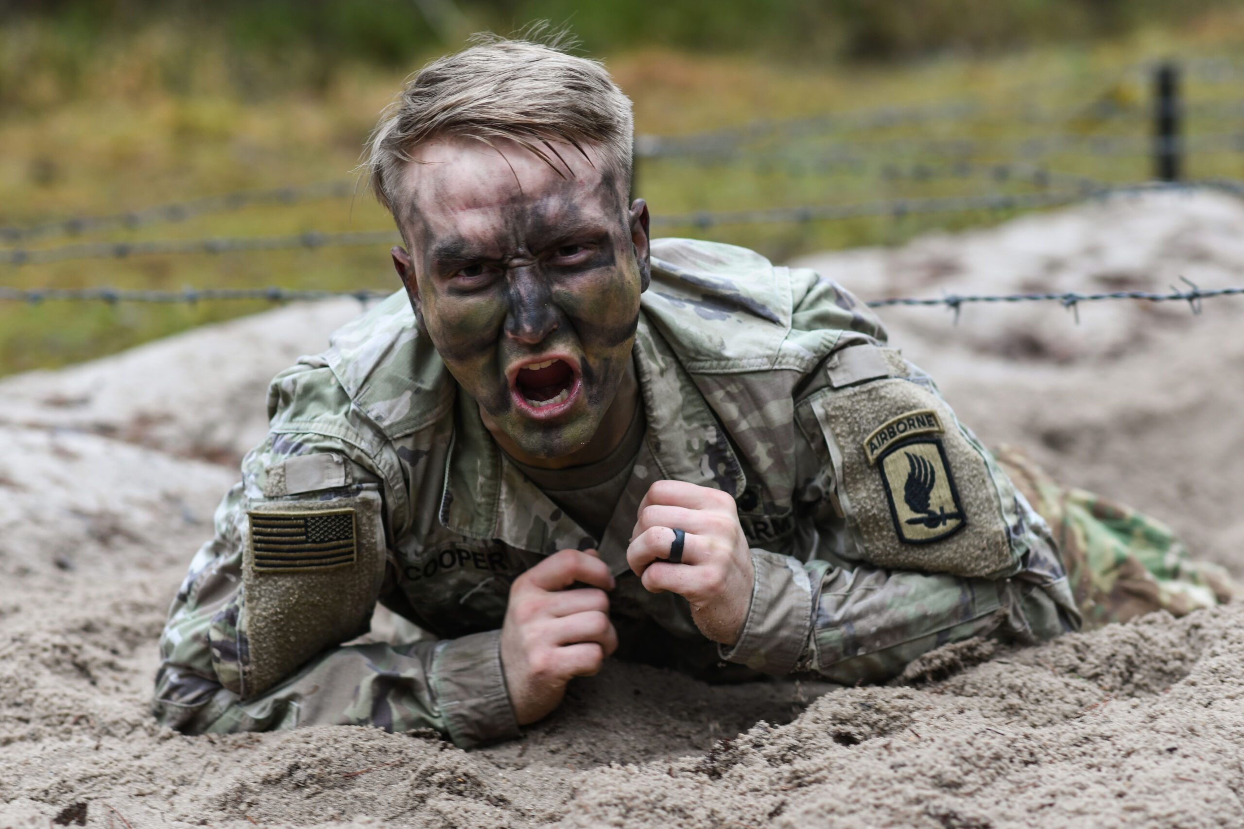 Airborne soldier completing an obstacle course in the sand. He is crawling under barbed wire obstacles