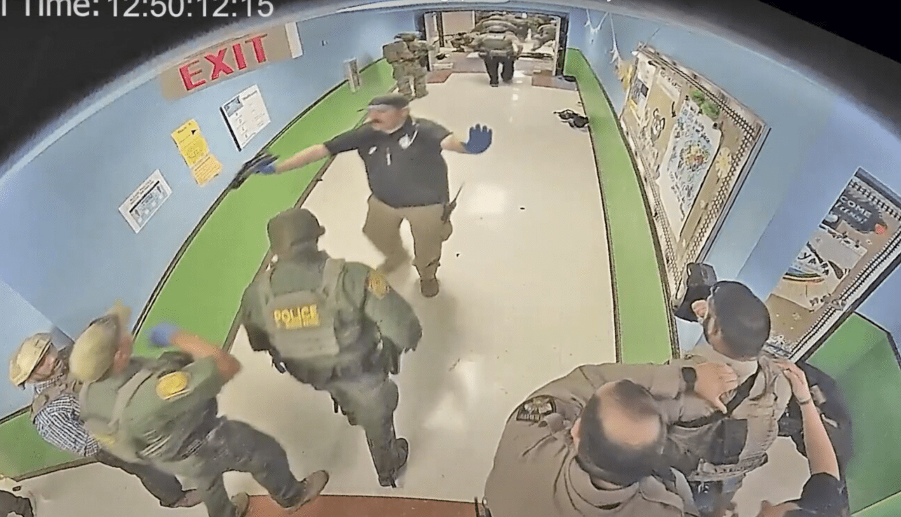 police officers in the hallway of Robb Elementary school being beckoned to "hold fast" in their positions by another law enforcement officer